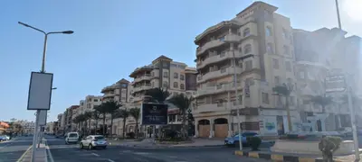 a building on a street with cars and palm trees at Florenza Khamsin Resort in Hurghada