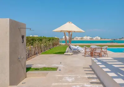 a patio with chairs and an umbrella and the water at Ancient Sands Gouna 4BR Villa Heated Pool & Lagoon in Hurghada