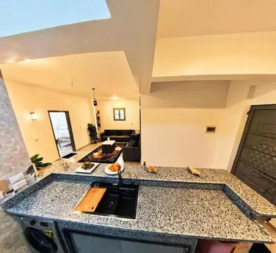 a kitchen with a counter top and a living room at Dreams By Mon in Al Karnak