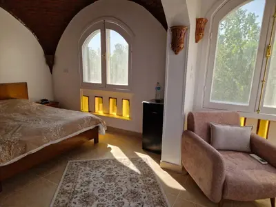 a bedroom with a bed and a chair and two windows at House Mountain Luxor - Villa for rent in Luxor