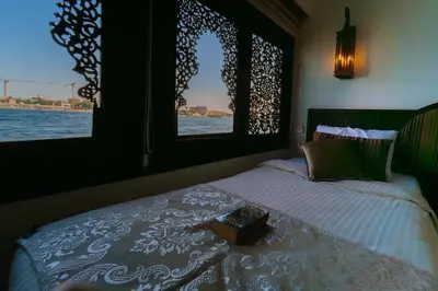 a bedroom with a bed with a window looking out over the water at Saphir Dahabiya luxury sailing boat Nile cruise Every Saturday from Luxor 4 or 7 nights in Luxor