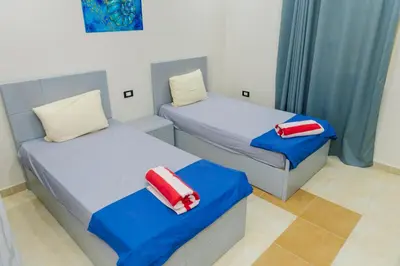 two beds in a room with blue and red pillows at Elaskary in Hurghada