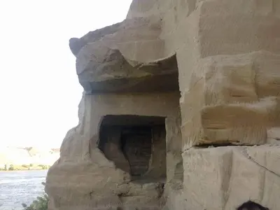 a stone building with a cave in the side of a river at Lucky Nile Tours in Luxor