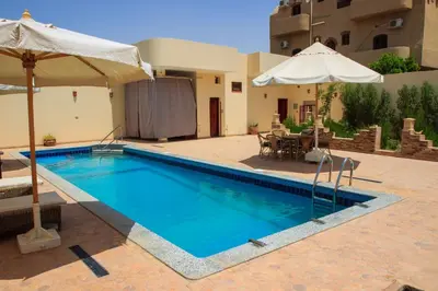 a swimming pool with an umbrella and a patio with a table at Riverbank House in Luxor