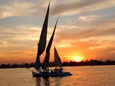 a boat with sails in the water at sunset at فلوكة نيلية in Luxor