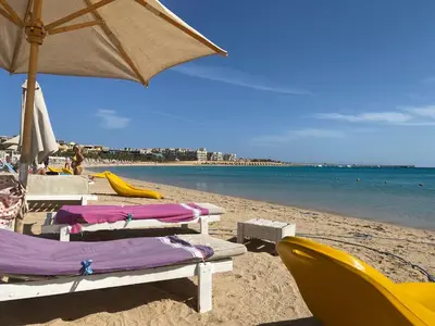 a beach with chairs and an umbrella and the ocean at Cozy Suite in Azzurra Resort Sahl Hasheesh 95 SqM in Hurghada