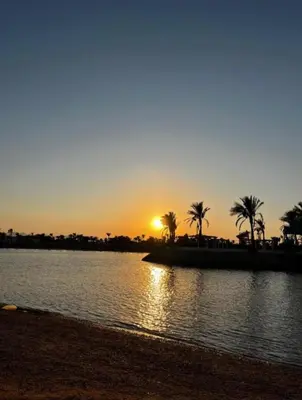 a sunset over a body of water with palm trees at Minaland Beach Resort & Aquapark in Hurghada