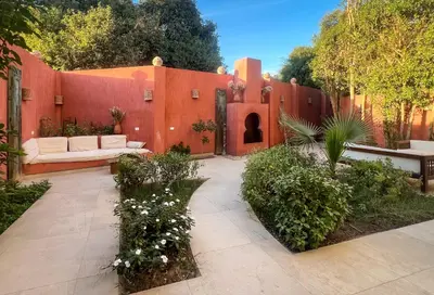 a garden with a red wall with a couch and a bench at Al Wadi Hotel in Al Aqālitah