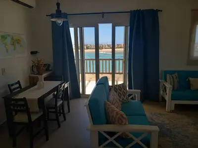 a living room with a blue couch and a table and a balcony at Blue Lagoon View - 2 Bed 2 Bath - Shared Pool - El Gouna in Hurghada