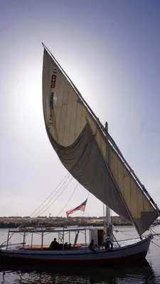 a small boat with a large sail on the water at Isis Nubian Services in Jazīrat Aswān