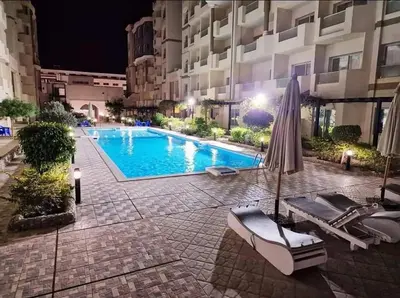 a swimming pool with an umbrella and chairs next to a building at Compound floranza in Hurghada