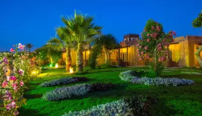 a garden with palm trees and flowers at night at Lilyland Beach Resort & Waterpark in Hurghada