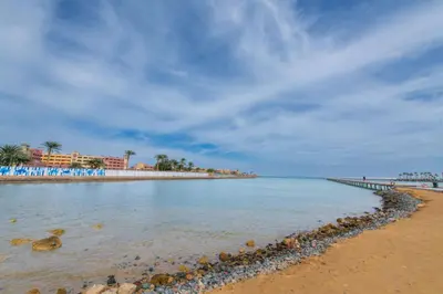 a beach with a pier and palm trees in the distance at Scandic Resort Hurghada مبني سكندك رزوت الغردقة in Hurghada