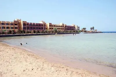 a beach with some people in the water and buildings at Taiba Golden Resort in Hurghada