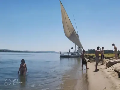 a group of people standing on the beach with a sail boat at sailboat in Luxor