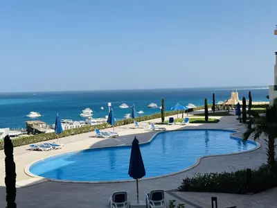 a swimming pool with chairs and umbrellas and the ocean at Beautiful Island View in Hurghada