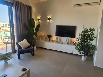 a living room with a flat screen tv and plants at Duplex 1BR King Bed and1 Sofa Bed By the Pool in Hurghada