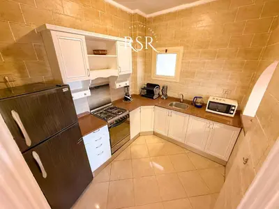 a small kitchen with white cabinets and a refrigerator at Apartment with a private roof top , pool , Garden in Hurghada
