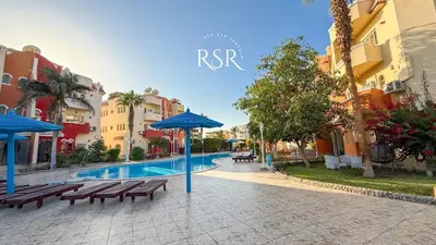 a pool with benches and umbrellas next to some buildings at Apartment with a private roof top , pool , Garden in Hurghada