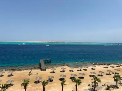 a beach with umbrellas and palm trees and the ocean at The Hill House in Hurghada
