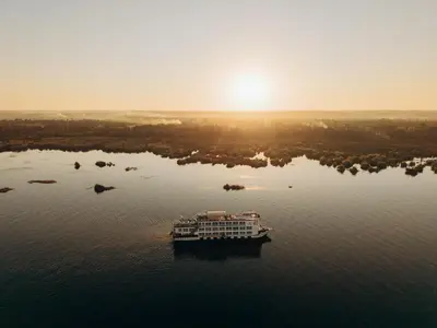 a boat on the water with the sun in the background at Savoy Yacht - Exclusive Nile Cruise from Luxor to Aswan in Luxor