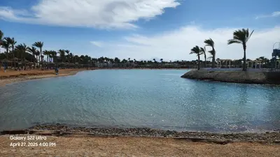 a large pool of water on a beach with palm trees at Chalet - Mirage Bay Resort & Aqua Park in Hurghada
