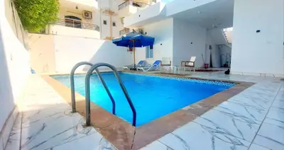 a swimming pool with an umbrella next to a building at Taha Guest house in Luxor