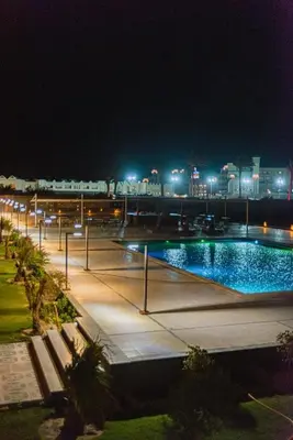 a swimming pool at night with a city in the background at luxury apartment with sea view in Hurghada