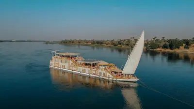 a boat with a sail in the water at Azhar Dahabiya luxury suites in Esna
