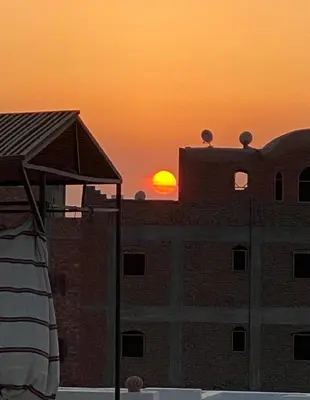 a sunset over a brick building with the sun in the distance at Maat Studio in Luxor