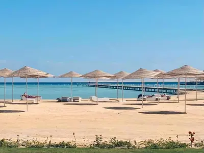 a beach with many straw umbrellas and the ocean at Modern loft overlooking downtown in Scandic Resort in Hurghada
