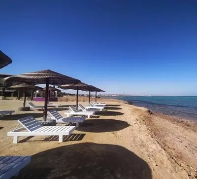 a row of white chairs and umbrellas on a beach at فنادير باي in Hurghada