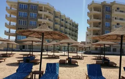 a beach with chairs and umbrellas in front of a building at Zafira Apartman in Hurghada