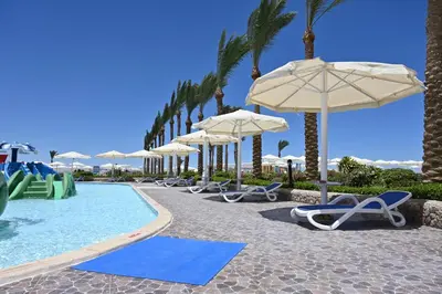 a pool with chairs and umbrellas and palm trees at Riviera Aqua Park Resort in Hurghada