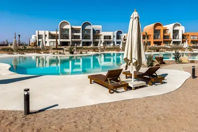 a swimming pool with two chairs and an umbrella at Cool & Curated 1BDR Kamaran El Gouna in Hurghada
