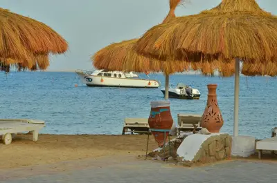 a beach with a straw umbrella and a boat in the water at Sun Beach Hotel ABO SOMA in Hurghada