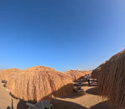 a row of straw umbrellas on a beach at Avenuo apartment in Hurghada