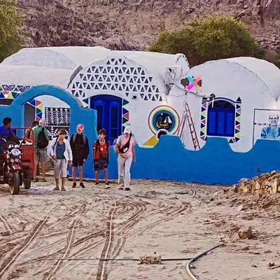 a group of people standing in front of a blue building at Kody doll in Jazīrat Suhayl