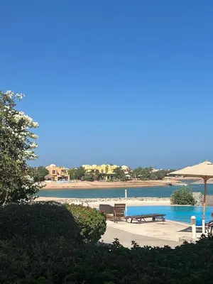 a pool with benches and an umbrella next to a beach at Cozy Lagoon Escpae-1Bdr Retreat in Hurghada