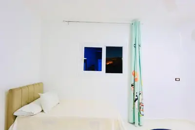 a white bedroom with a bed and a window at Memnon House in Al Karnak