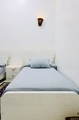 a bedroom with a white bed with a blue blanket at Memnon House in Al Karnak