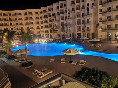 a swimming pool with chairs and umbrellas in front of a building at Princess Resort in Hurghada