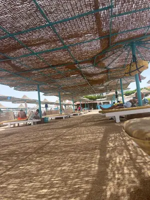a large straw umbrella on a beach with benches at Hurghada Studios in Hurghada