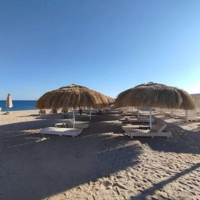 a row of chairs and straw umbrellas on a beach at Luxury Suite Princess Resort Two bedroom apartment Hurghada سويت فاخر البرنسيسه غرفتين in Hurghada