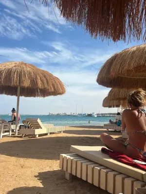 a woman in a bikini sitting on a beach with umbrellas at Luxury Suite Princess Resort Two bedroom apartment Hurghada سويت فاخر البرنسيسه غرفتين in Hurghada