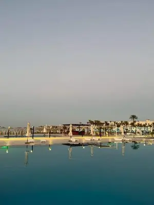 a pool of water with chairs and umbrellas on a beach at منتجع سكانديك الغردقة in Hurghada