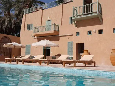 a pool with chairs and umbrellas next to a building at Habu Hotel in Al Aqālitah