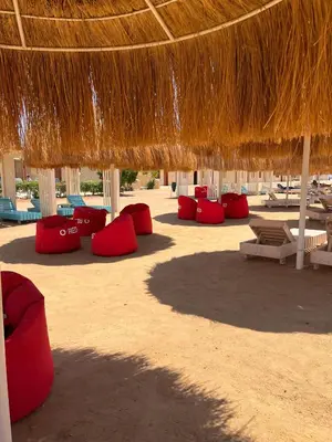 a beach with red chairs and a straw umbrella at Hurgada New studio in Avenue on Mamsha -private beach&pool in Hurghada