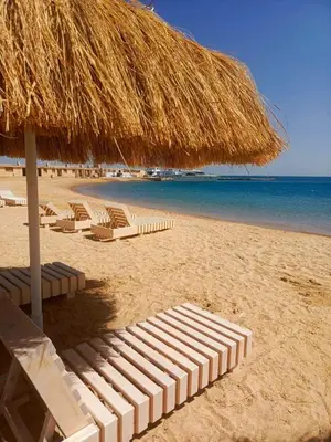 a group of lounge chairs and a straw umbrella on a beach at Hurgada New studio in Avenue on Mamsha -private beach&pool in Hurghada