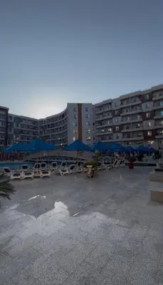 a parking lot with chairs and blue umbrellas at Hurghada Tiba Golden Resort Apartment Strand Pool 22 in Hurghada